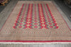 Load image into Gallery viewer, A large rectangular area rug with a traditional geometric pattern, featuring red, beige, and blue diamond motifs, laid out on a gray wooden floor.
