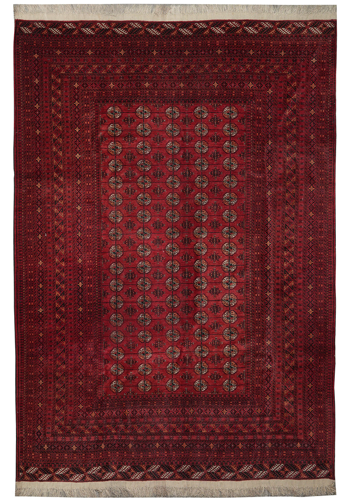 A traditional rectangular area rug with a deep red field, featuring a central panel of repeating medallion motifs and a detailed border, finished with cream-colored fringe on the top and bottom edges.