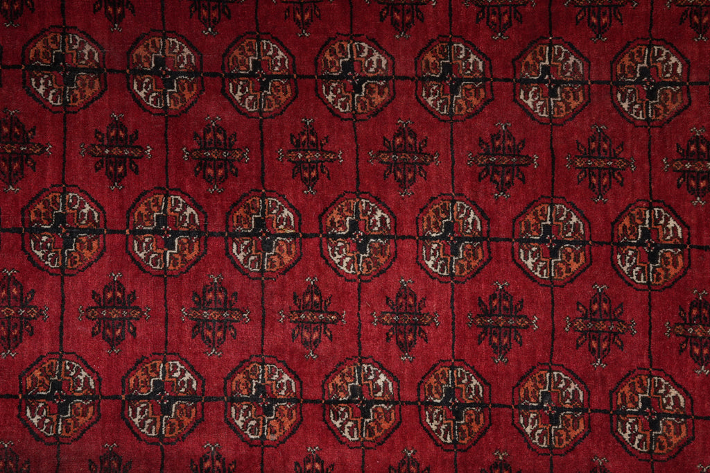 A close-up of a red patterned textile or rug showing repeated circular medallion motifs and dark geometric borders in black, brown, and beige.