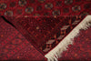 Load image into Gallery viewer, A close-up of a red patterned rug with geometric and floral motifs, featuring cream fringe on one corner.
