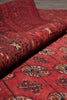 Load image into Gallery viewer, A close-up of a folded red patterned rug showing detailed motifs in beige, black, and brown on a red base.