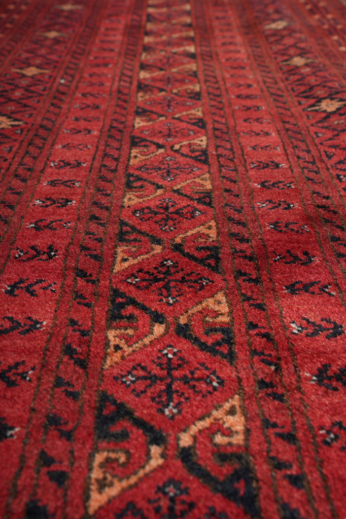 A close-up of a red patterned rug with geometric and tribal-style motifs in black, beige, and brown.