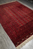 Load image into Gallery viewer, A traditional red wool area rug with a geometric pattern and beige fringe, shown laid out on a gray concrete floor.