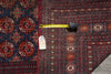 Load image into Gallery viewer, A close-up of a patterned area rug with a dark navy blue field on the left and a deep red field on the right, featuring intricate geometric and medallion motifs in beige, rust, and brown. A yellow tape measure and a white tag are placed horizontally across the rug to indicate scale and identify the product.