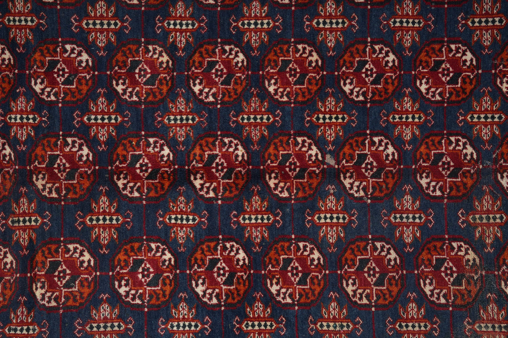 A close-up of a patterned textile or rug showing a repeating medallion motif in red, rust, cream, and dark blue.
