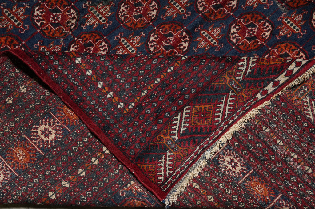 A folded patterned textile, likely a rug or scarf, showing a dark navy blue base with red, orange, and cream geometric and floral motifs, finished with a fringed edge.