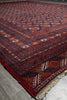 Load image into Gallery viewer, A traditional Persian-style area rug with a deep red field, navy blue borders, and intricate geometric and floral motifs in orange, cream, and black, laid out on a gray tiled floor.