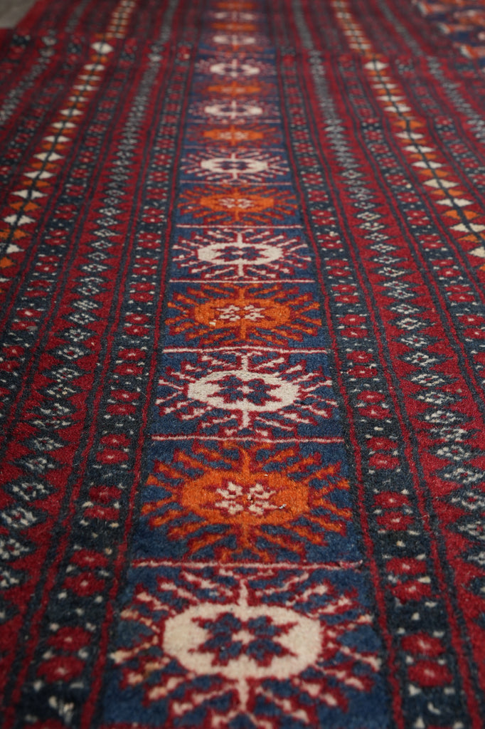 A close-up of a patterned rug with geometric and floral motifs in red, navy blue, orange, and cream, showing the detailed woven texture.