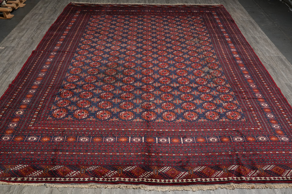 A large traditional Persian-style area rug with a dark navy blue field, red and orange floral motifs, and a detailed geometric border, laid out on a gray concrete floor.
