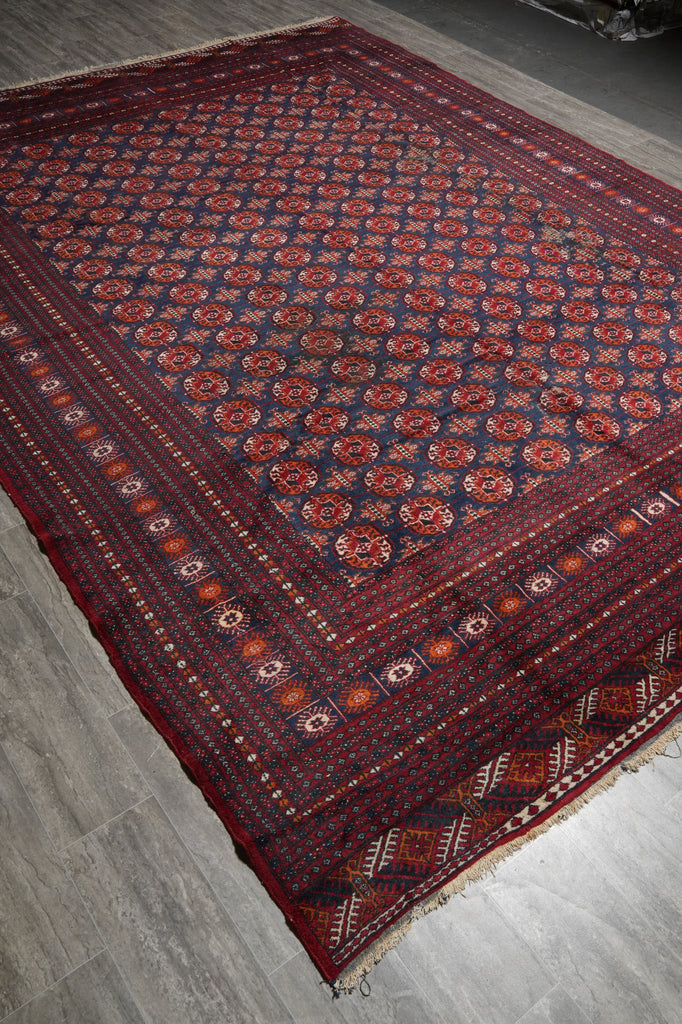 A traditional patterned area rug with a deep red border and navy blue field, laid out diagonally on a gray wood-look floor.