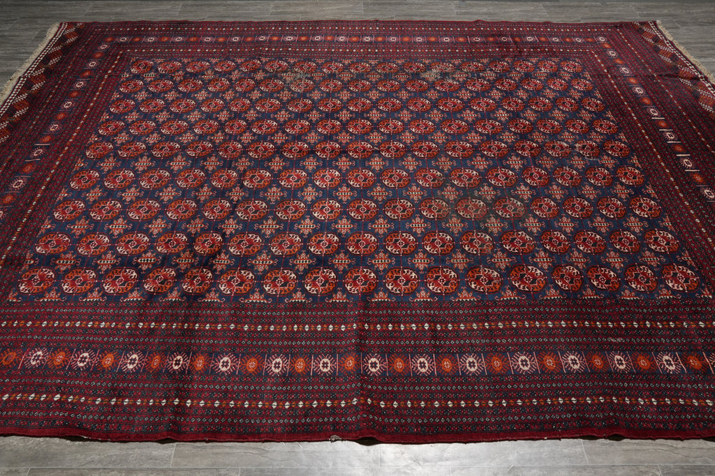A large rectangular area rug with a dark navy blue field, repeating red and orange floral medallions, and a patterned border, laid flat on a gray tiled floor.