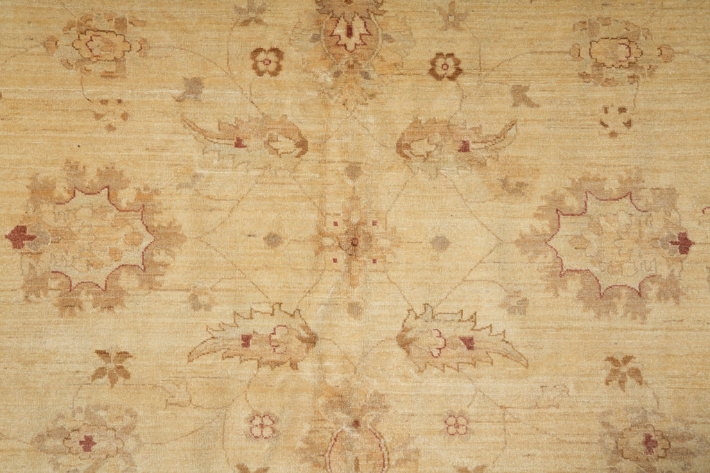 A close-up of a beige and tan patterned rug with a faded floral and medallion design in muted brown and dusty red tones.