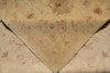 Load image into Gallery viewer, A close-up of a folded vintage area rug with a faded floral and scroll pattern in muted beige, tan, and dusty rose tones.