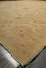 Load image into Gallery viewer, A close-up of a beige area rug with a subtle traditional floral pattern in muted brown and tan tones, showing the textured pile and a frayed edge.
