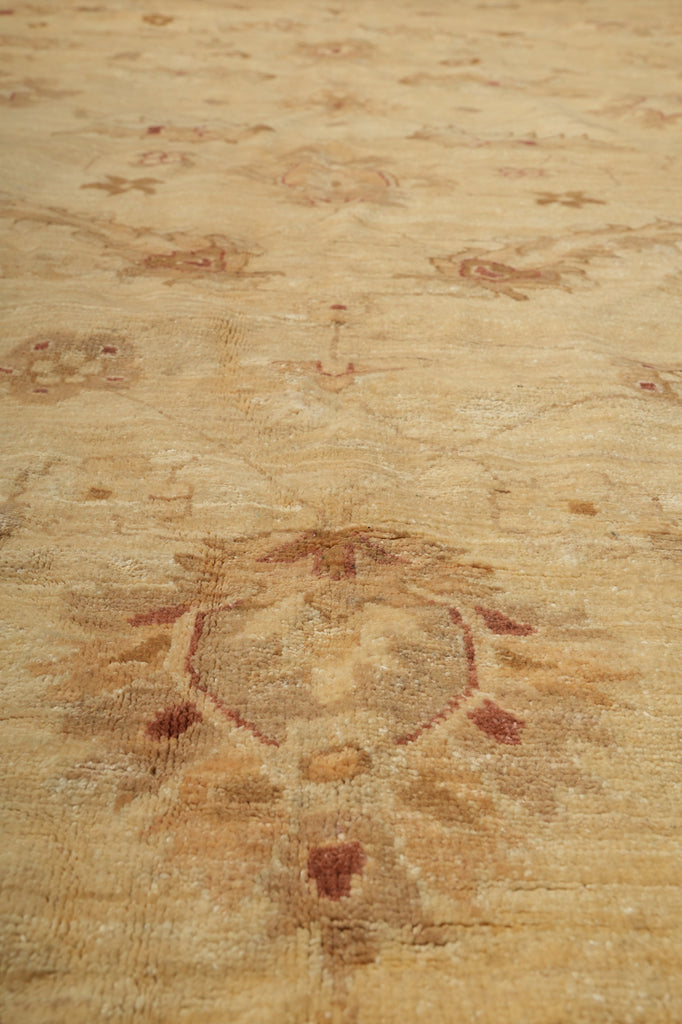 A close-up of a light beige rug with a faded sunburst motif in muted brown and reddish accents.