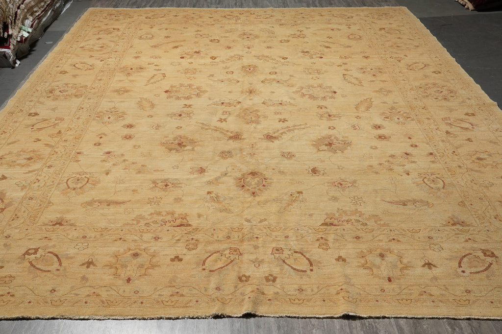 A large beige area rug with an intricate traditional floral and paisley pattern in warm tan and brown tones, laid out on a dark floor.
