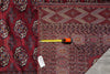 Load image into Gallery viewer, A detailed view of a traditional Persian-style area rug with a deep red field, geometric diamond motifs, and a dark navy border, shown with a tape measure and size tag to indicate size.