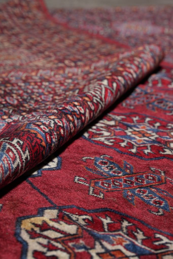 A close-up of a folded red patterned rug showing detailed woven motifs in blue, cream, and brown.