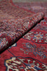 Load image into Gallery viewer, A close-up of a folded red patterned rug showing detailed woven motifs in blue, cream, and brown.