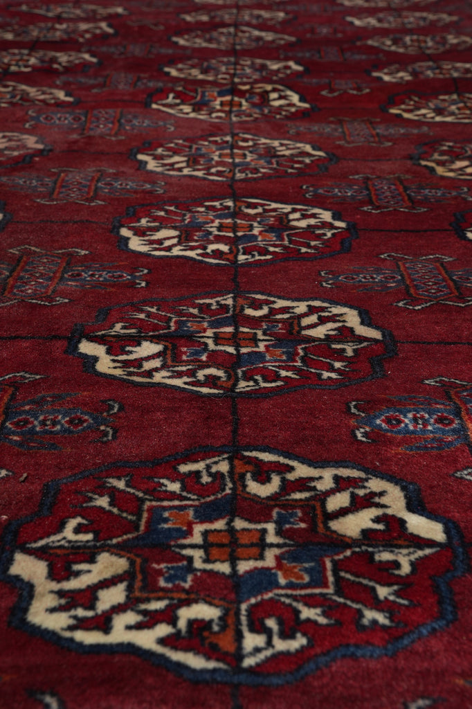 A close-up of a red patterned rug with repeating medallion motifs in cream, blue, and rust tones.