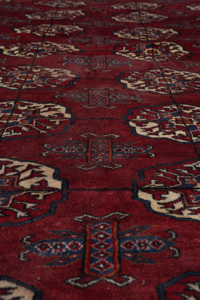 A close-up of a red patterned rug with repeating geometric and floral motifs in beige, blue, and brown.
