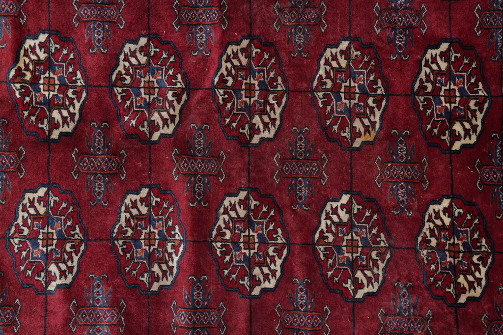 A close-up of a traditional patterned rug featuring a deep red field with repeating beige medallions and dark blue geometric accents.