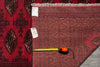 Load image into Gallery viewer, A close-up of a red patterned area rug with a tape measure and size tag laid on it, next to another darker patterned rug.