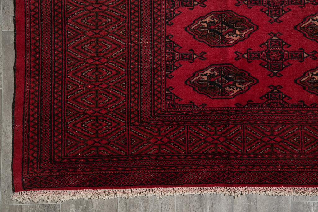 A close-up of a red and black patterned rug showing the detailed geometric borders and fringe.