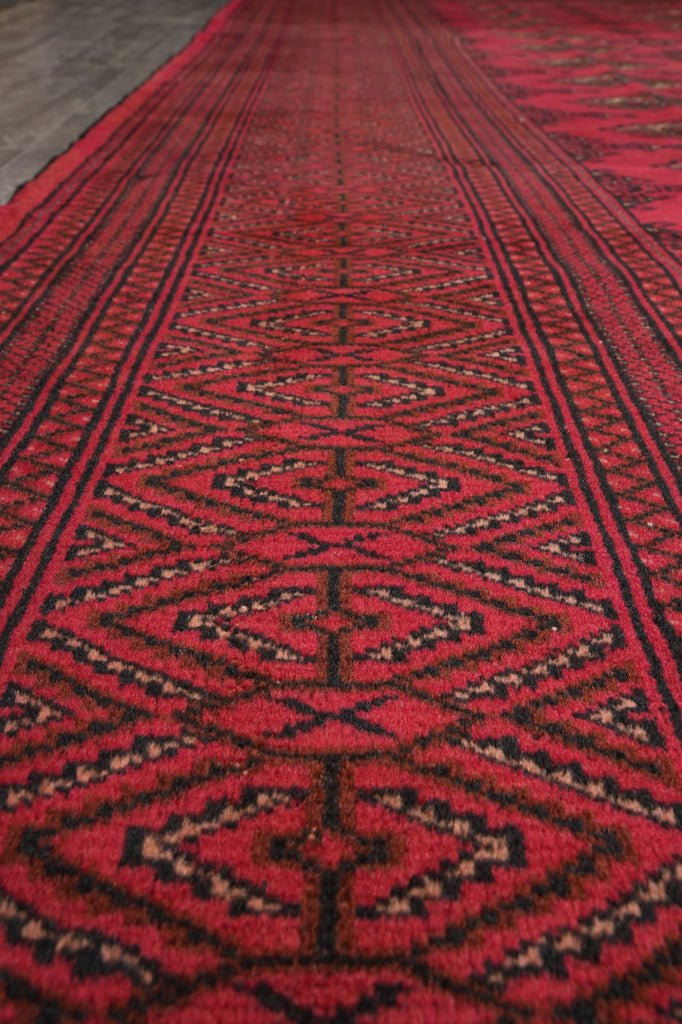 A close-up view of a red patterned rug with geometric tribal designs in black and beige, shown in perspective.