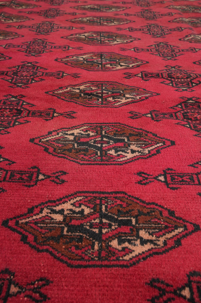 A close-up of a red patterned rug with traditional geometric and floral motifs in dark brown, beige, and black.