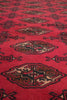 Load image into Gallery viewer, A close-up of a red patterned rug with traditional geometric and floral motifs in dark brown, beige, and black.