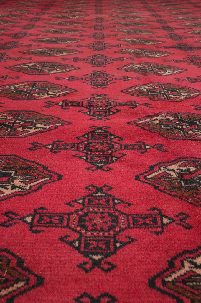 A close-up view of a red patterned rug with geometric medallion motifs in black, beige, and brown.