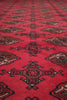 Load image into Gallery viewer, A close-up view of a red patterned rug with geometric medallion motifs in black, beige, and brown.
