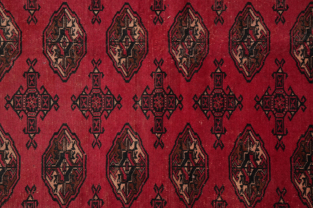 A close-up of a red patterned textile or rug featuring repeating geometric medallion motifs in black, beige, and muted brown.