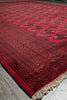 Load image into Gallery viewer, A red patterned rug with dark borders and cream fringe, photographed at an angle on a gray floor.