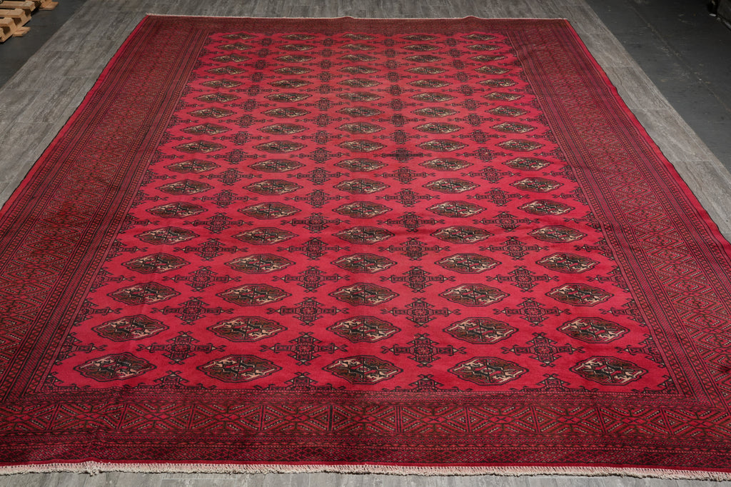 A large red oriental area rug with a repeating geometric pattern and dark borders, laid out on a gray floor.