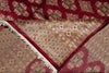 Load image into Gallery viewer, A close-up of a patterned area rug showing its deep red border, beige and brown geometric center, and white fringe tassels.