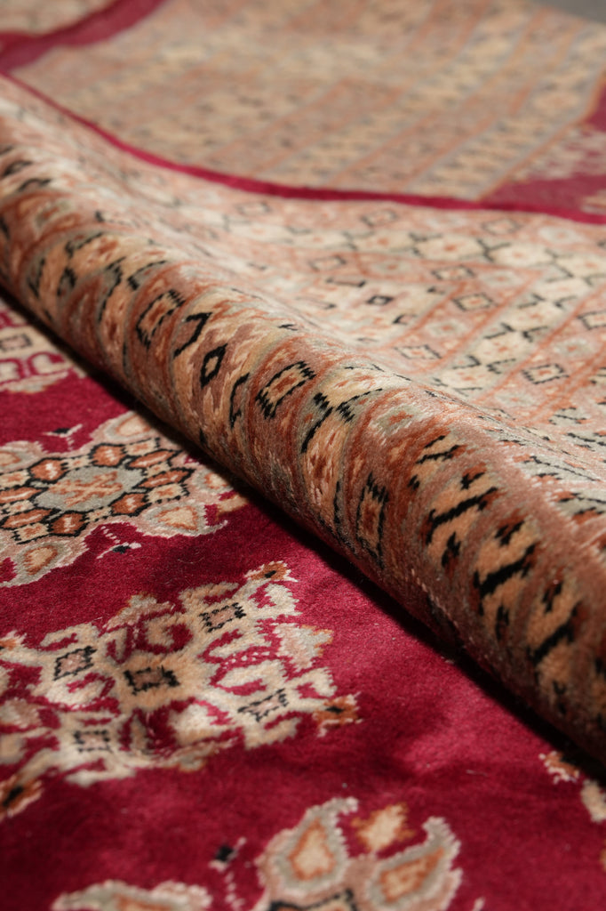 Close-up of a patterned area rug showing a deep red field with cream floral motifs and a central beige and brown border with black detailing.
