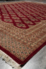 Load image into Gallery viewer, A traditional patterned area rug with a deep red border, cream and rust base, and geometric motifs, shown on a gray tiled floor.