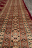 Load image into Gallery viewer, A close-up of a patterned area rug with horizontal bands of geometric motifs in terracotta, beige, black, and muted red, with a solid dark red border visible along the bottom right.
