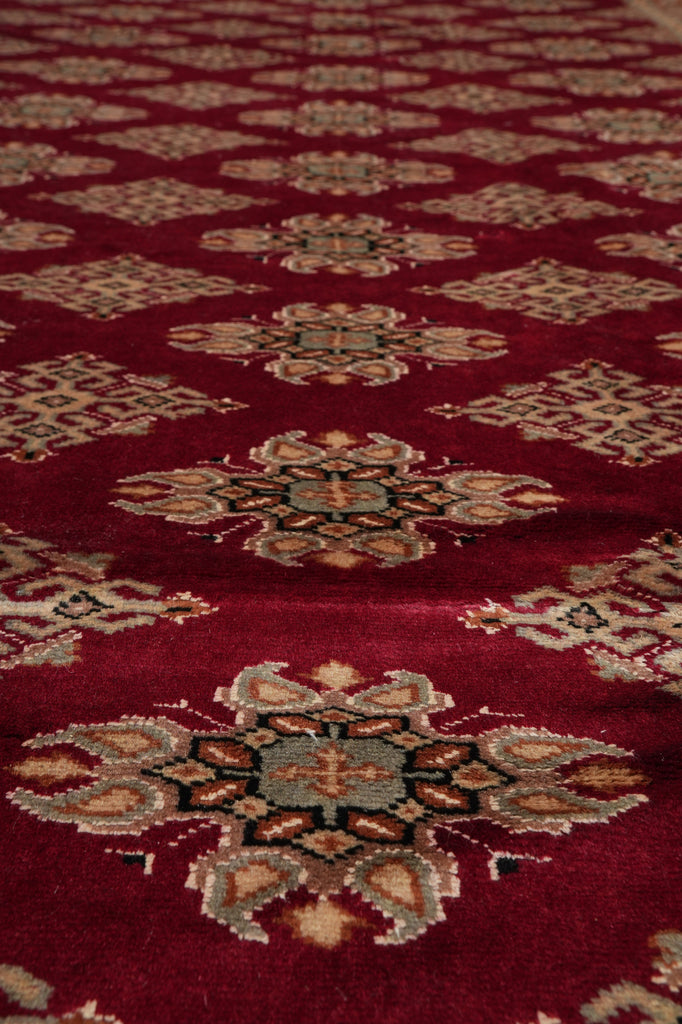 A close-up of a red patterned rug with ornate medallion motifs in beige, brown, and muted blue-gray.