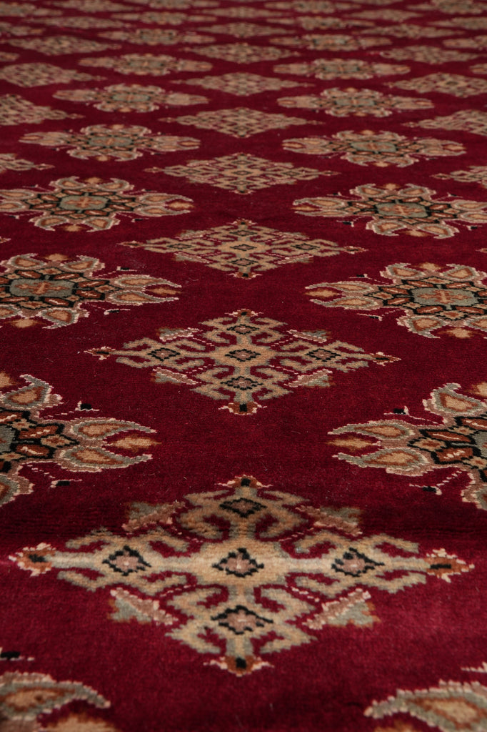A close-up of a red patterned rug or textile with repeating diamond motifs in beige, black, and muted green.