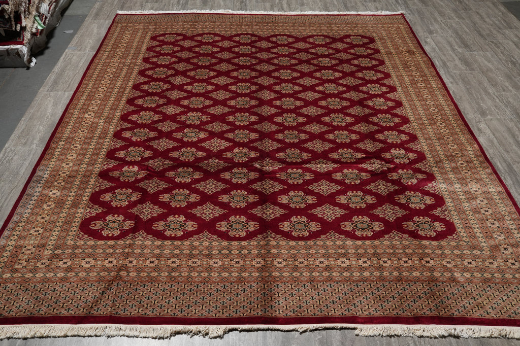 A rectangular area rug with a traditional Persian-style pattern, featuring a deep red central field with geometric medallions and a beige outer border, laid out on a gray floor.