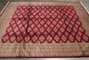 Load image into Gallery viewer, A large rectangular area rug laid flat on a gray floor, featuring a bold red geometric lattice pattern over a beige and brown ornate field with a patterned border.