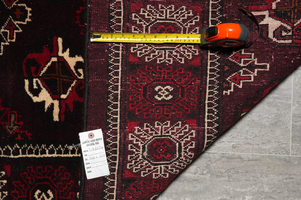 A close-up of a patterned area rug with a measuring tape and a price tag placed on top, showing the rug's design and dimensions against a gray tile floor.