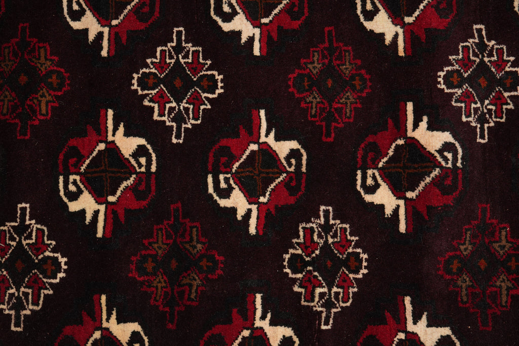 A close-up of a woven textile with a repeating geometric pattern in dark red, cream, and black on a very dark background.
