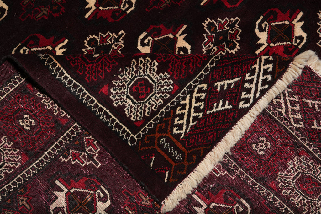 A close-up of a patterned rug showing deep red, burgundy, cream, and brown geometric and floral motifs with a fringed edge.