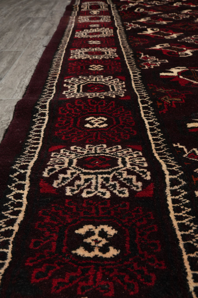 A close-up view of a traditional oriental runner rug with a dark red and black base, featuring cream and red geometric patterns and motifs.