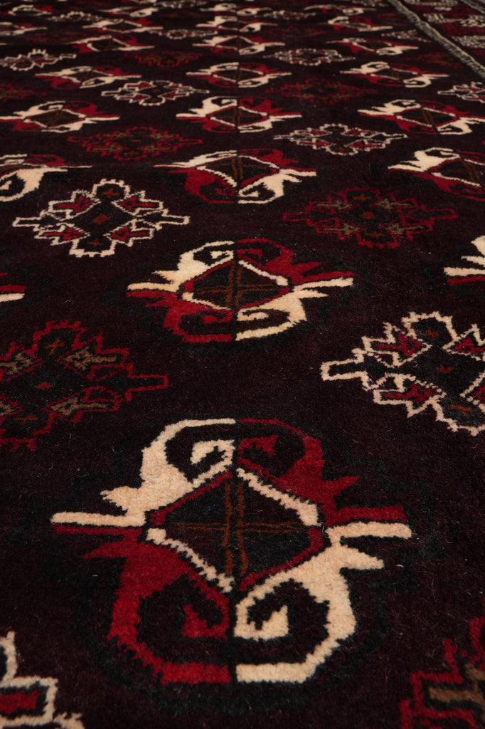 A close-up of a patterned rug with a dark brown or near-black base, featuring red and cream geometric and floral motifs.