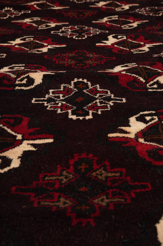 A close-up of a patterned textile or rug with a dark base and repeating geometric motifs in red, cream, and black.